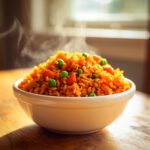 A white bowl overflowing with hot, steaming spanish rice mixed with bright green peas and diced carrots.