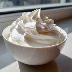 Close-up of stiff, glossy white peaks resembling whipped topping, likely royal icing recipe consistency, in a small white bowl.