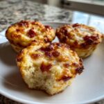 Three golden-brown Pizza Muffins on a white plate, one with a bite taken out showing the fluffy interior.