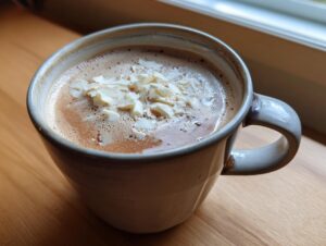 A close-up of a mug filled with rich white hot chocolate, topped with white chocolate shavings.