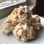 A stack of four homemade avalanche cookies, made with cereal and marshmallows, dusted with powdered sugar.