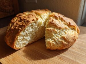 A freshly baked round of soda bread, cut open to show the soft interior, resting on a wooden cutting board.