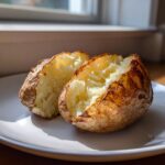 A perfectly cooked air fryer baked potato, split open to show the fluffy interior, resting on a white plate.