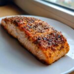 A close-up of a perfectly cooked, seasoned fillet of air fryer salmon resting on a white plate.