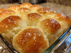 Close-up of shiny, golden brown soft rolls baked together in a glass dish.