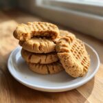 A stack of freshly baked peanut butter cookies with classic crosshatch marks, one cookie has a bite taken out.