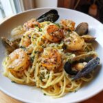 A close-up of creamy seafood pasta featuring perfectly seared shrimp, mussels, and clams, garnished with parsley.
