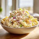 Close-up of a large bowl filled with creamy Tuna Pasta Salad featuring rotini pasta, tuna, red onion, and celery.