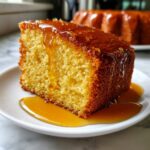 A close-up of a moist slice of Bacardi rum cake being drizzled with golden rum glaze on a white plate.