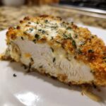 Close-up of a slice of baked ranch chicken showing juicy white meat, crispy breading, and melted cheesy ranch topping.