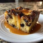 A close-up of a rich slice of bread pudding with raisins, generously drizzled with bourbon sauce.