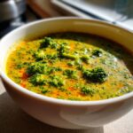 Close-up of a white bowl filled with creamy, vibrant broccoli cheddar soup featuring bright green florets.