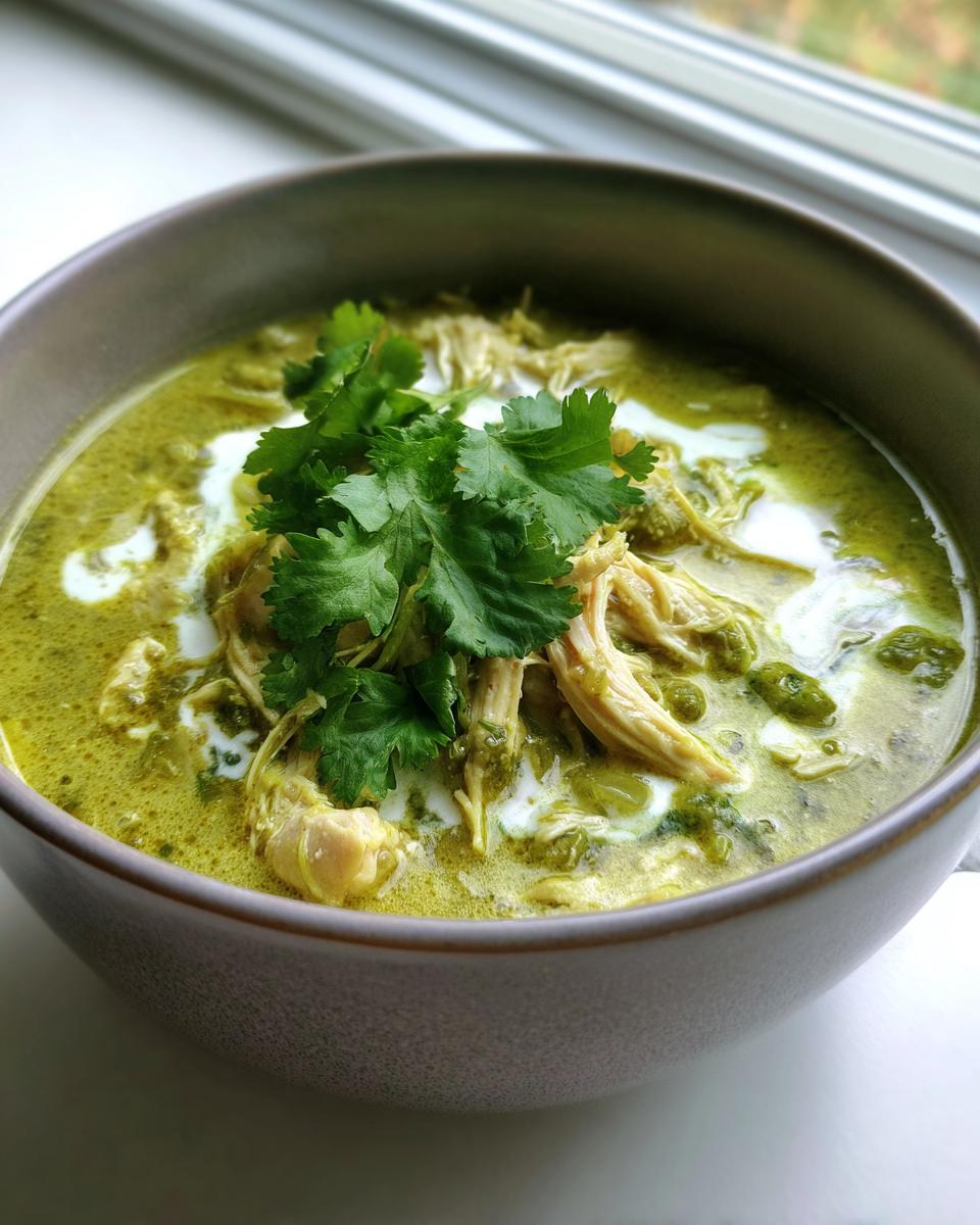 Close-up of a bowl containing creamy green chicken poblano soup, topped with shredded chicken, cream, and fresh cilantro.