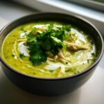 Close-up of a vibrant green chicken poblano soup recipe, topped with shredded chicken, crema swirls, and fresh cilantro.
