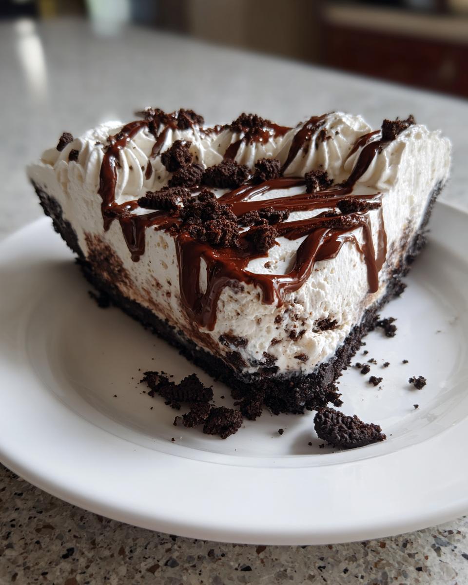 A generous slice of chocolate cookie ice cream pie topped with whipped cream, chocolate fudge drizzle, and cookie crumbs.