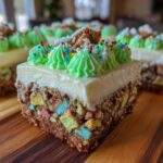 Close-up of a slice of christmas tree cheesecake featuring a colorful cereal base, white topping, and green piped frosting with sprinkles.
