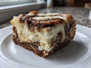 A close-up of a decadent slice of cinnamon roll cheesecake showing rich cinnamon swirls and creamy texture on a white plate.