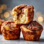 A stack of three golden brown french toast muffins coated in cinnamon sugar, with the top one broken open showing the fluffy interior.