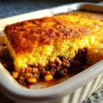 A close-up of a square serving of cowboy cornbread casserole showing the thick, golden cornbread topping over a savory ground meat and corn filling.