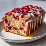 A close-up of a moist cranberry orange bread loaf topped with white glaze and fresh cranberries.