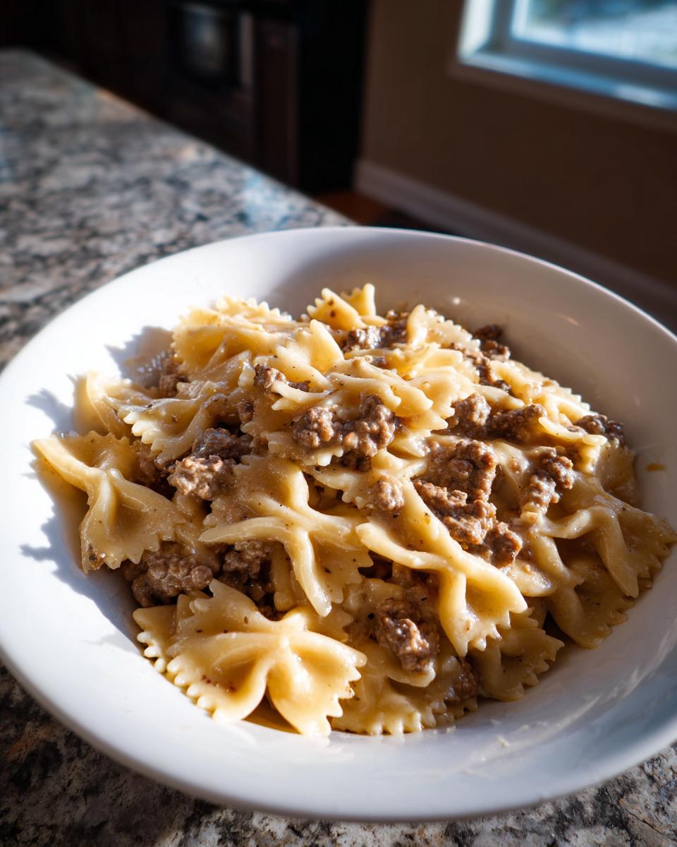 A white bowl filled with creamy beef pasta made with bowtie noodles and seasoned ground beef.