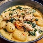 Close-up of a hearty bowl of creamy gnocchi soup featuring shredded chicken, wilted spinach, and herbs.