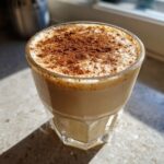 Close-up of creamy eggnog topped with a dusting of cinnamon in a faceted glass.