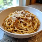 A close-up of a white bowl filled with creamy french onion pasta topped with caramelized onions and grated Parmesan cheese.