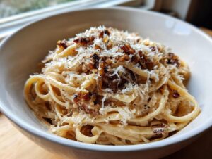 A close-up of a bowl of creamy french onion pasta, generously topped with grated Parmesan cheese and caramelized onions.