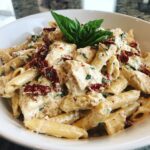 Close-up of creamy Marry Me Chicken Pasta featuring penne, chicken chunks, sun-dried tomatoes, and basil garnish.