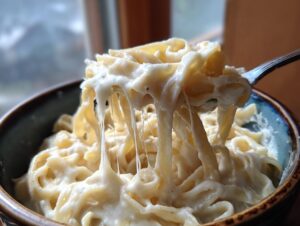 Close-up of fettuccine pasta coated in creamy olive garden alfredo sauce being lifted by a fork, showing cheese pull.