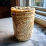 A creamy jar of overnight oats, visible through a Ball mason jar, topped with chia seeds, ready for breakfast.