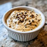 Close-up of rich, creamy peppercorn sauce topped with whole black peppercorns in a white ramekin.