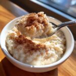 A spoonful of creamy rice pudding recipe topped generously with ground cinnamon, served in a white bowl.