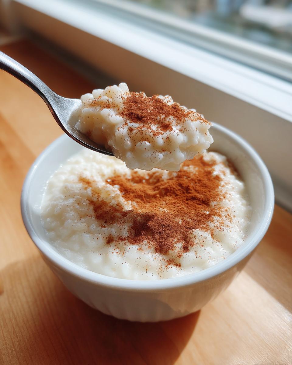 A spoonful of creamy rice pudding recipe topped with cinnamon being lifted from a white bowl.