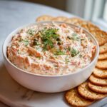 A white bowl filled with creamy smoked salmon dip, garnished with fresh dill and capers, served with crackers.