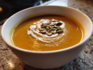 A close-up of a bowl of rich, orange squash soup garnished with pumpkin seeds and a swirl of cream.