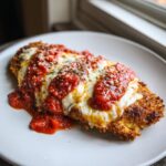 A close-up of a crispy breaded chicken parmesan recipe cutlet topped with melted mozzarella and rich marinara sauce.