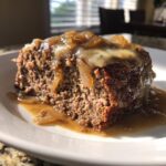 A close-up slice of moist crockpot french onion meatloaf topped with melted cheese and caramelized onions in brown gravy.