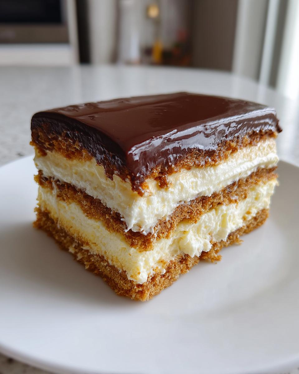 A single, rich slice of eclair cake featuring layers of graham cracker, vanilla cream filling, and topped with shiny chocolate ganache.