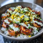 A close-up view of a vibrant shrimp bowl featuring grilled shrimp over rice, topped with avocado, corn salsa, and a creamy cilantro dressing.