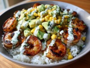 Close-up of a vibrant shrimp bowl featuring grilled shrimp over rice, topped with avocado, corn, and a creamy white sauce.