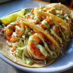 Close-up of three delicious shrimp taco shells filled with slaw, seasoned shrimp, and drizzled with a creamy green sauce.