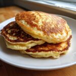 A close-up stack of three golden-brown almond flour pancakes served on a white plate.