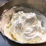 Close-up of freshly whipped, fluffy vanilla buttercream frosting inside a stainless steel mixing bowl.