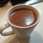 Close-up of a rich, dark french hot chocolate with a foamy top in a white ceramic mug.