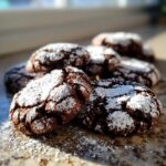 A close-up of several fudgy chocolate crinkle cookies heavily dusted with white powdered sugar.