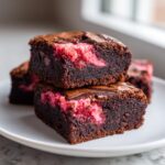 Close-up of stacked, fudgy strawberry brownies showing the rich chocolate base and bright pink strawberry swirl filling.