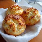 Three freshly baked, golden brown cloud bread buns resting in a white paper-lined basket.