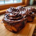 Close-up of gooey chocolate cinnamon rolls generously covered in chocolate frosting and mini chocolate chips.